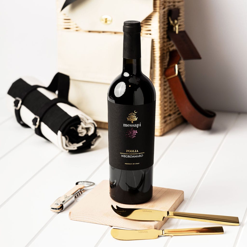 Messapi Italian wine, gold cheese knives, beech wooden board, bottle opener, a striped picnic rug with a portable wicker basket. 