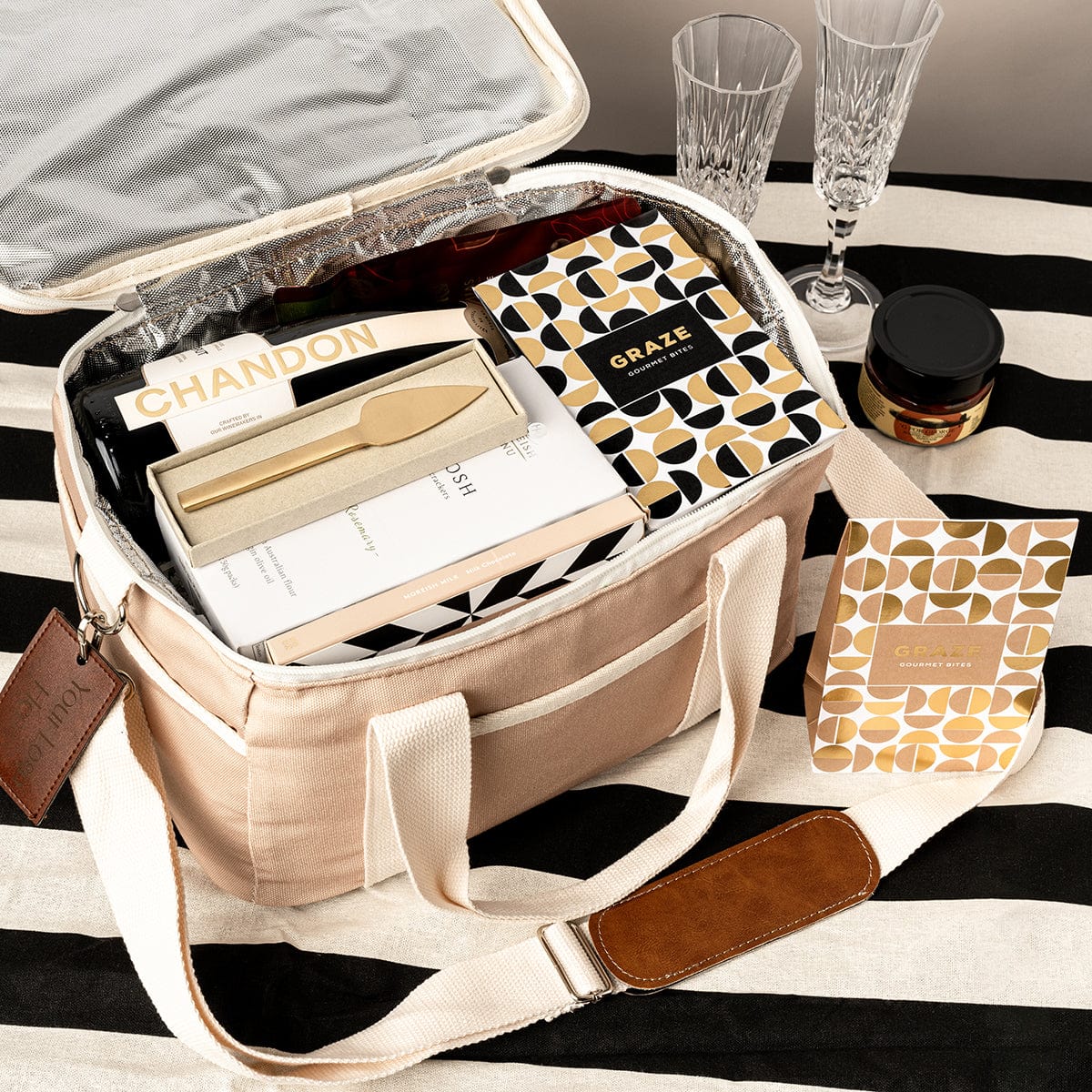 Taupe cooler bag gift with acrylic champagne flutes, Chandon, capsicum tapenade, brass gold cheese knife, and a selection of gourmet snack items.