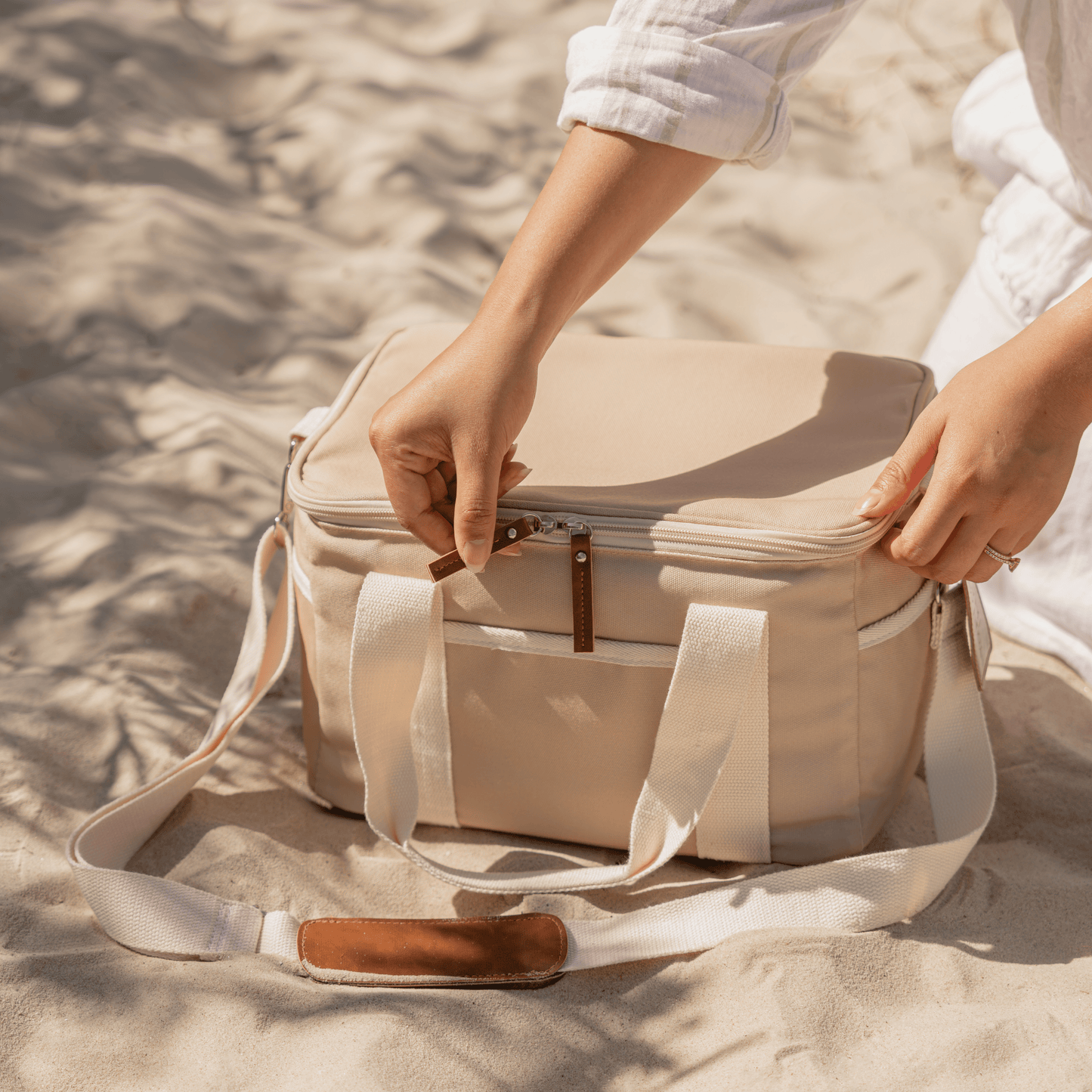 Woman zipping a taupe cooler bag at the beach. 